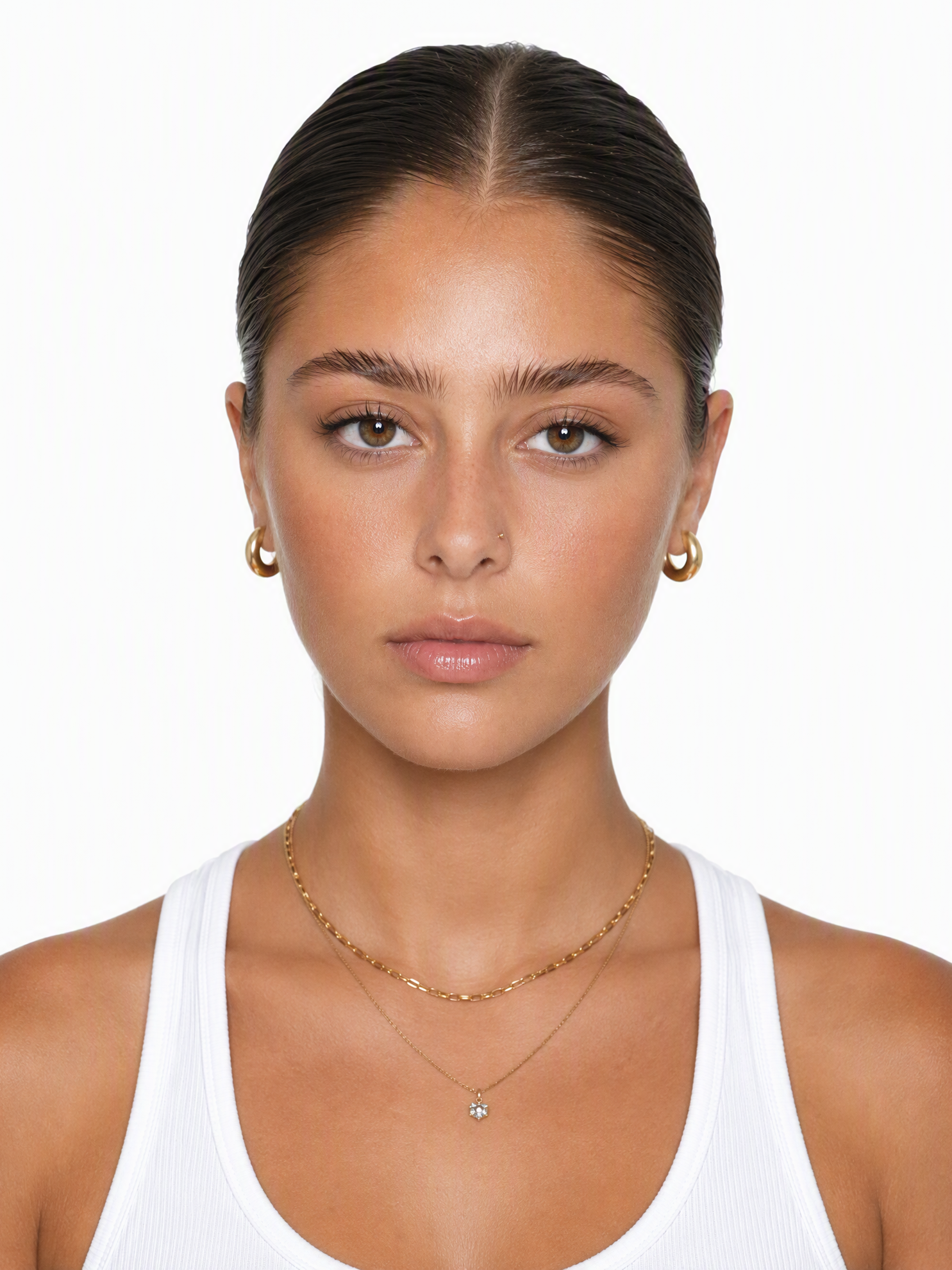 A young female fashion model with slicked-back dark hair, gold hoop earrings and necklace, medium shot, plain white background, studio lighting, photo-realistic.